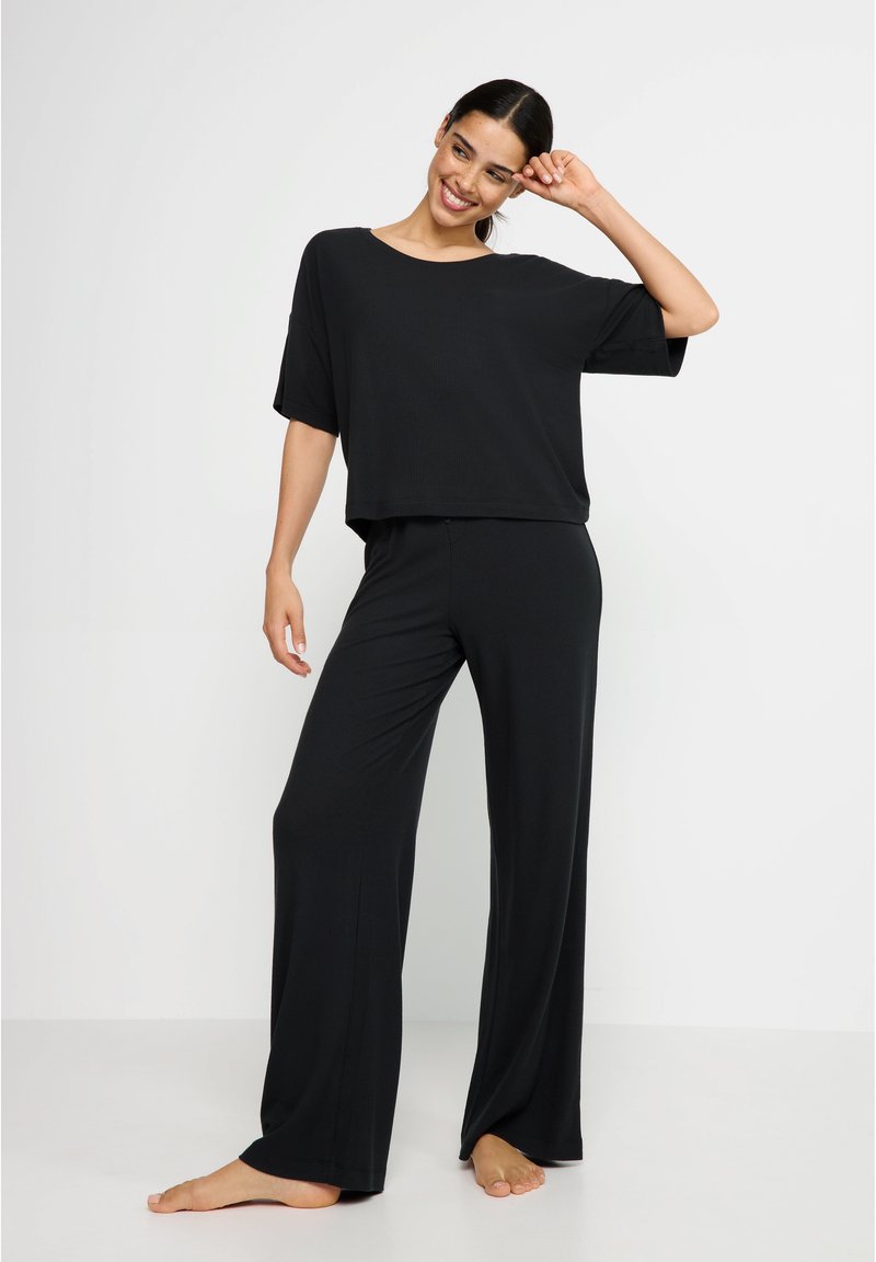 Fekete loungewear szett, amely egy lazán illeszkedő, rövid ujjú felsőből és széles szárú nadrágból áll, puha, könnyű anyagból, sima textúrával.