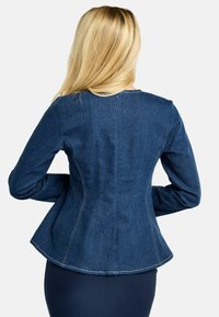 Temno modra denim jakna, krojena z razširjenim robom, izrazitimi šivi in dolgimi rokavi. Pogled od zadaj razkriva oblikovne linije in teksturo materiala.