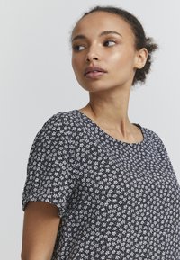 Haut à motifs floraux noir et blanc à manches courtes, col rond et texture de tissu douce. Le design présente de petites fleurs sur un fond sombre.