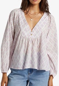 Blus med blommönster i lätt tyg; har en djup V-ringning, knapprad och långa ärmar med elastiska manschetter. Vit botten med rosa och lila blommor.