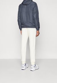 Mörkgrå huva jacka med elastiska ärmar, ihop med krämfärgade joggers. Vita sneakers har marinblå detaljer och strukturerade sulor.