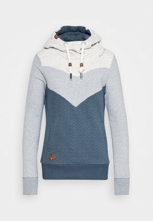 Sweat à capuche avec haut blanc, manches gris clair, corps bleu foncé à motif chevrons, capuche avec cordon de serrage et petite pièce marron près de l’ourlet.