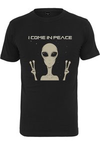T-shirt noir présentant un graphisme d'un extraterrestre avec de grands yeux, faisant un signe de paix, et le texte "JE VIENS EN PAIX" au-dessus en blanc.