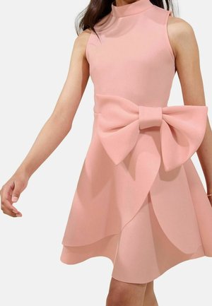Robe rose sans manches avec un col montant, ornée d'un grand nœud décoratif à la taille et de détails de jupe à étages.