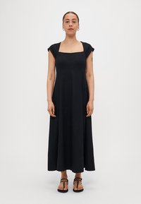 Čierne ľanové maxi šaty so štvorcovým výstrihom, krátkymi rukávmi a vzdušným strihom. Outfit dopĺňajú jednoduché čierne žabky.