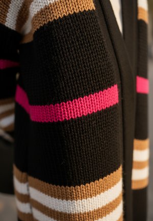 Dzianinowy kardigan w kolorze czarnym z poziomymi paskami w kolorze beżowym, białym i fuksjowym. Posiada teksturowany materiał i dekolt w kształcie litery V.