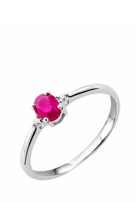 Anello d'argento con un centro in rubino ovale, affiancato da due piccole pietre trasparenti, che mostra una fascia elegante con finitura lucida.