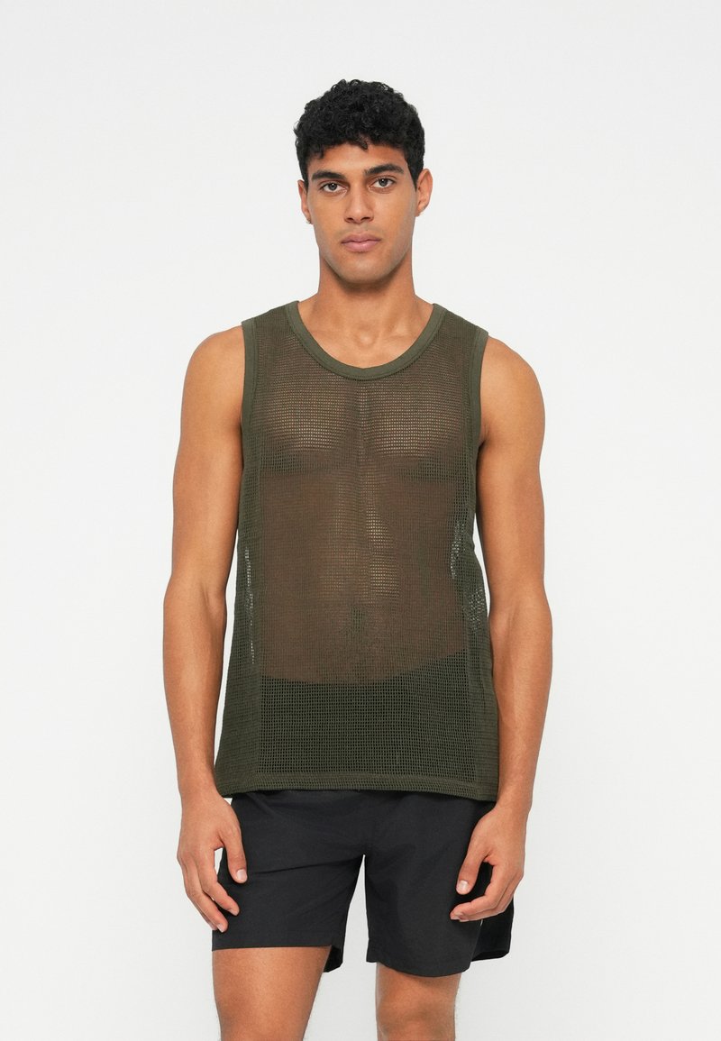 Top a rete verde oliva con scollatura rotonda, caratterizzato da una vestibilità ampia e un tessuto testurizzato. Abbinato a pantaloni corti neri.