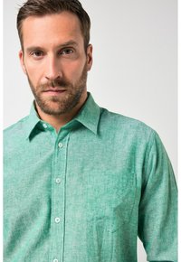 Groen overhemd met korte mouwen en knopen, gemaakt van gestructureerde stof met een voorzak en een klassieke kraag. Heeft lichtgroene knopen.