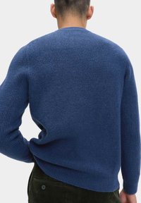 Modrý pletený svetr s texturovaným vzorem, kulatým výstřihem a mírně volným střihem. Materiál vypadá měkký a teplý.