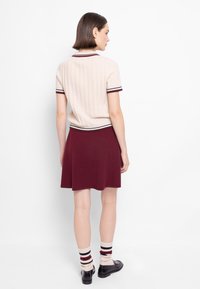 Maglione a maniche corte a coste in beige chiaro con rifiniture bordeaux, abbinato a una gonna svasata bordeaux e calzini a righe beige e bordeaux.