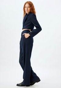 Marineblauw gestreepte cropped blazer met lange mouwen, gecombineerd met hoge taille, wijde pijpen. De stof lijkt glad en geknipt.