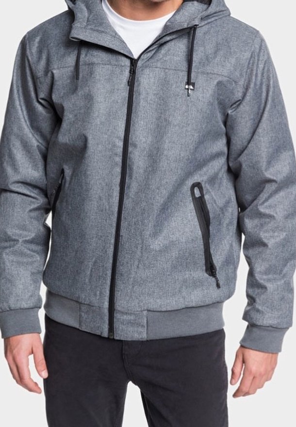Homme portant un sweat à capuche zippé gris clair avec cordons de serrage et poches zippées, associé à un pantalon noir.