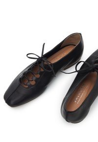 Černé kožené baleríny na šněrování s hranatou špičkou a béžovou stélkou s nápisem "BALACAN" na bílém pozadí.