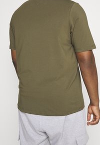 Zadní pohled na osobu oblečenou v olivově zeleném tričku s krátkým rukávem a světlých šortkách s cargo kapsami.