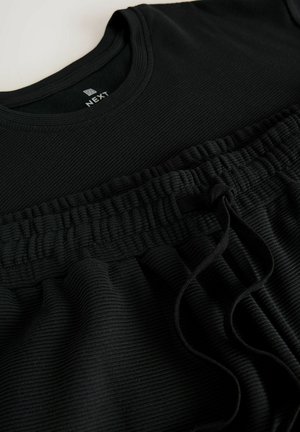 Top nero a coste con vita elastica e dettaglio con cordoncino, caratterizzato da una superficie testurizzata e un scollatura morbida. Adatto per l'abbigliamento casual.
