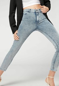 Jeans de tiro alto en azul claro con un ajuste slim, que presentan una textura desgastada, lazos para el cinturón y un diseño clásico de cinco bolsillos, combinados con un blazer negro.