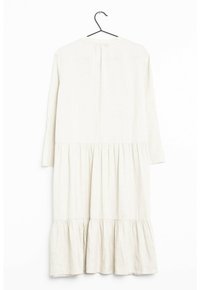 Lång, krämfärgad linnekjol med rund halsringning, långa ärmar och volangkant. Enkel design med en samlad midjedetalj.