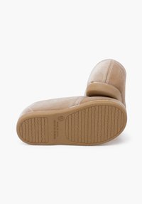 Scarpe slip-on in suede beige con una superficie liscia, punta arrotondata e suola in gomma con un motivo a ondine; etichettate "Made in Spain."