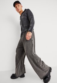 Grau gestreiftes Langarmoberteil und lose graue Hose aus strukturiertem Stoff; klobige schwarze Schuhe mit Gummisohle.
