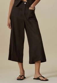 Černé lněné culottes s širokým střihem, obsahující přední kapsy a zapínání na knoflík, v kombinaci s černými žabkami.