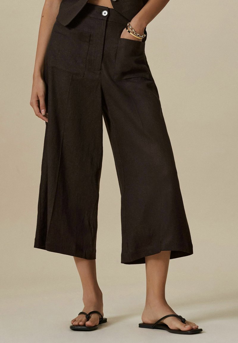 Černé lněné culottes s širokým střihem, obsahující přední kapsy a zapínání na knoflík, v kombinaci s černými žabkami.