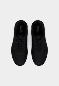 Ζευγάρι μαύρα vegan αθλητικά παπούτσια με κορδόνια, φαίνονται από πάνω σε απλό ανοιχτό γκρι φόντο.