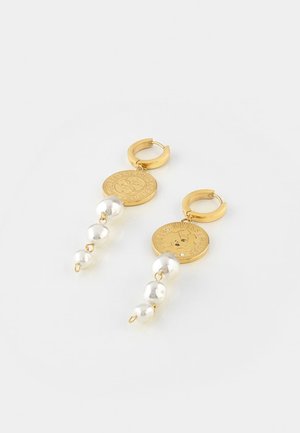 Gouden creolen met hangende gouden muntbedels en drie aflopende witte parels aan elke oorbel tegen een eenvoudige lichte achtergrond.