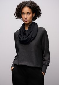 Czarny szalik z pętlą zarzucony na ciemnoszary, teksturowany sweter z szerokimi, luźnymi rękawami. Do stroju dobrano czarne spodnie.