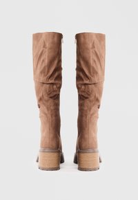 Bocanci din suede maro până la genunchi, cu un design lejer, având vârful rotund și toc stivuț cu striații. Închidere cu fermoar la spate.