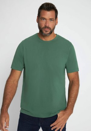 Zielony t-shirt z krótkim rękawem z gładkiego materiału bawełnianego. Okrągły dekolt, luźny krój, z prostym dołem. Noszony z ciemnoniebieskimi dżinsami.