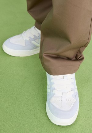 Világoskék és fehér sportcipők velúr és hálós anyagból, fehér fűzővel és textured talppal, barna nadrággal párosítva.
