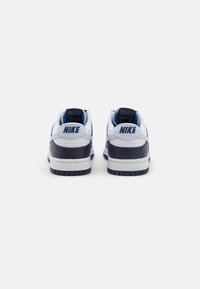 Białe i granatowe sneakersy Nike z skórzaną cholewką, wyściełanym kołnierzem i gumową podeszwą. Logo "NIKE" w ciemnoniebieskim kolorze na pięcie i języku.