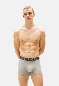 Calzoncillos ajustados de hombre en gris con una cinturilla negra que presenta una marca blanca. Material suave con un diseño ceñido y detalles de costura en contraste.