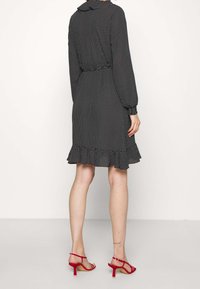 Vestido de lunares en blanco y negro con mangas largas, dobladillo con volantes y cintura ajustada. Combinado con sandalias de tacón rojas.