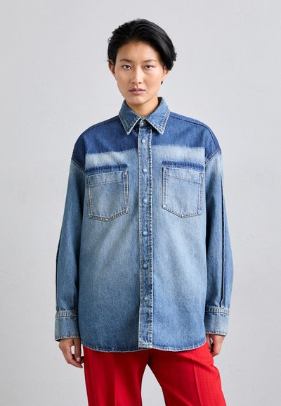 Light blue denim shirt with a button-down front, contrast shoulder panel, and two chest pockets. Features a relaxed fit and soft texture.
