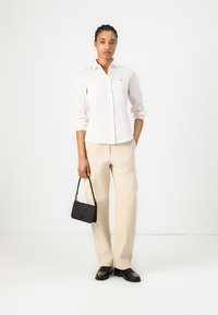 Lichtroze overhemd met lange mouwen, beige wijde broek en zwarte handtas. Zwarte schoenen met textuurdetails maken de outfit compleet.