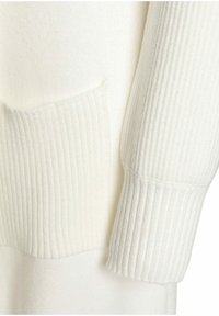 Biały sweter dziany, z detalem w postaci ściągacza na mankiecie i kieszeni. Tekstura jest miękka, z różnorodnymi wzorami dzianiny.