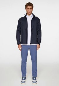 Marinblå vindjacka med dragkedja, vit pikétröja, blå byxor och blå sneakers. Mjukt tyg; avslappnad passform; minimalistisk design.