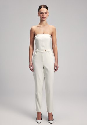 Hvid stropløs jumpsuit med skræddersyet pasform, sidelommer og en frontknap. Glat tekstur med en skræddersyet silhuet, parret med spidse hæle.