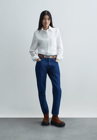 Valge pika varrukaga nööpidega särk peene kortsuga, tumedasinine kõrge vöökohaga teksad, pruunid pahkluu saapad ja Moschino vöö.