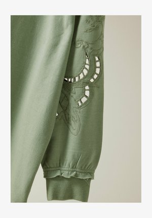 Zielona bawełniana bluza z haftowanym wzorem, z wycięciami na rękawach i falbaną u mankietów. Miękka w dotyku.