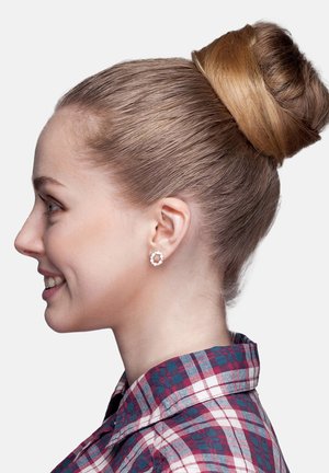 Orecchini rotondi in tonalità argento con piccole pietre trasparenti incastonate in un design floreale. Capelli acconciati in un bun alto e liscio. Camicia a quadri rossi e blu.