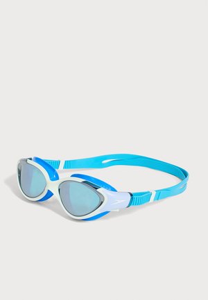 Lunettes de natation avec verres teintés bleus, montures blanches et bleues, et une sangle bleue réglable sur un fond clair.