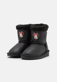 Bottes noires pour enfants avec une finition brillante, doublure en fourrure noire douce, et un patch Minnie Mouse avec un nœud rouge à pois sur le côté.