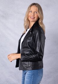 Black leather motorcycle jacket with a fitted silhouette, zippered pockets, and a snap collar. Worn over a white top and denim jeans.