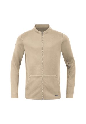 Beige Zip-Jacke mit hohem Kragen, ausgestattet mit zwei Fronttaschen und Branding entlang des Reißverschlusses. Weicher Stoff mit glatter Textur.