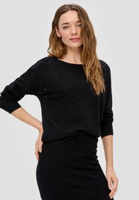 Zwarte gebreide sweater met een zigzagpatroon, ronde halslijn en driekwartmouwen. De stof heeft een gestructureerd, ademend ontwerp.