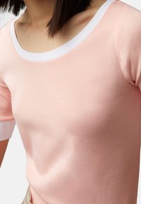 Světle růžový top s krátkým rukávem a bílým kulatým výstřihem. Měkká textura s hladkým povrchem, s přiléhavým střihem a kontrastními manžetami.