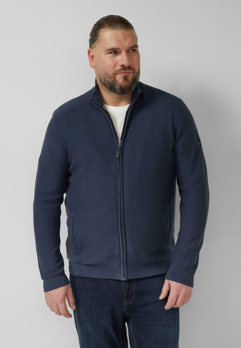 Marineblauwe trui met ritssluiting en getextureerde details op de schouders, geribde manchetten en zoom, gemaakt van een zachte stof. Gecombineerd met een donkere jeans.